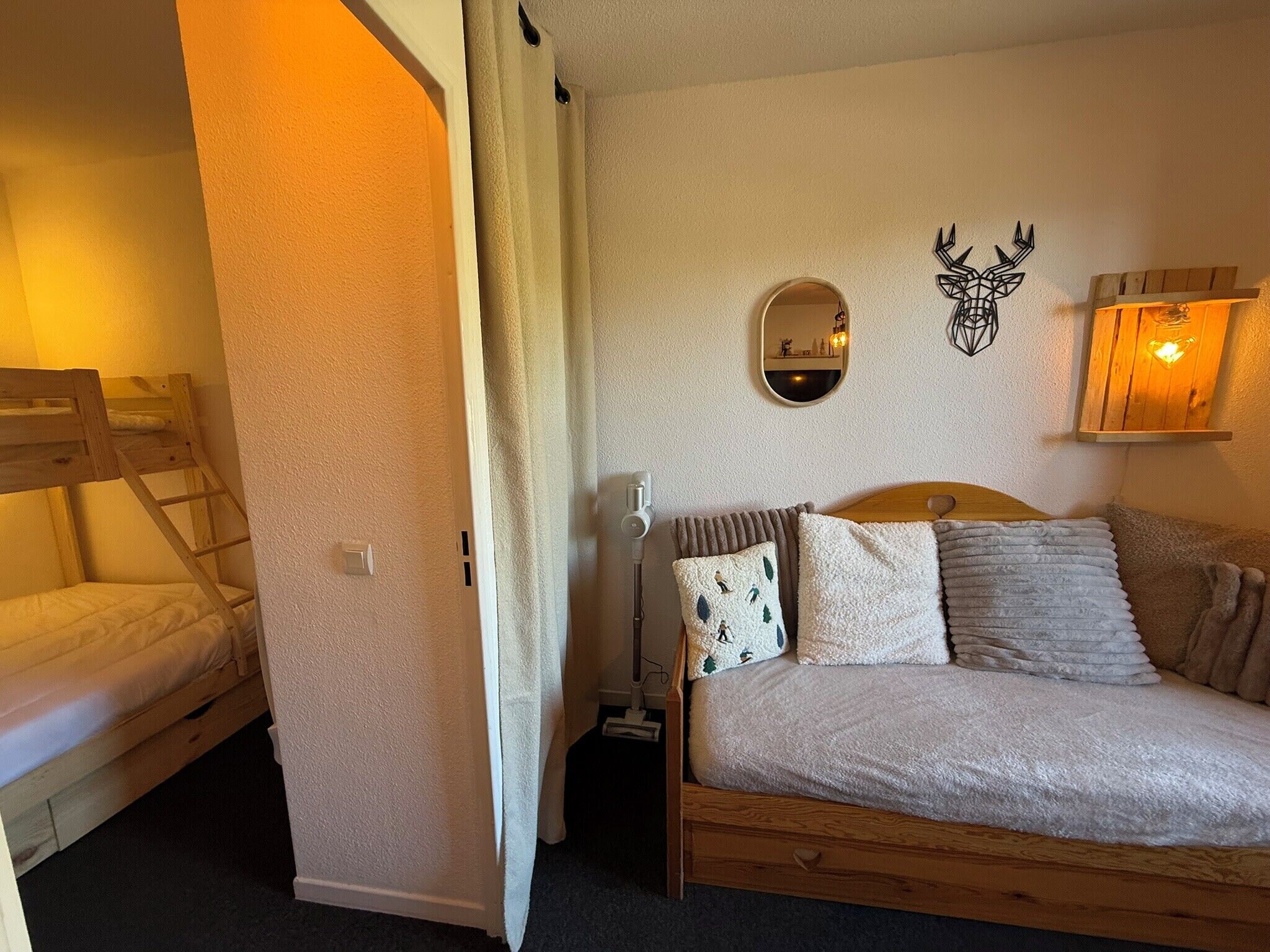 A bedroom with a bunk bed, a single bed, a mirror, a wall-mounted light, and a decorative deer head.