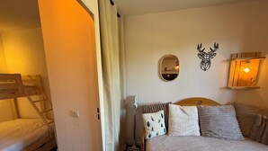 Une chambre avec un lit superposé, un lit simple, un miroir, une lampe fixée au mur et une tête de cerf décorative.