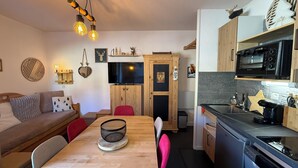 Un espace de vie compact comprenant une table à manger en bois, un canapé, une cuisine équipée d’une cuisinière et d’un lave-vaisselle, ainsi qu’une télévision.