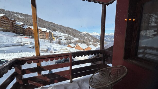 Un balcon offrant une vue sur un paysage montagneux enneigé, avec des balustrades en bois et un fauteuil en osier.
