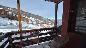 A balcony with a view of a snowy mountain landscape, wooden railings, and a wicker chair.