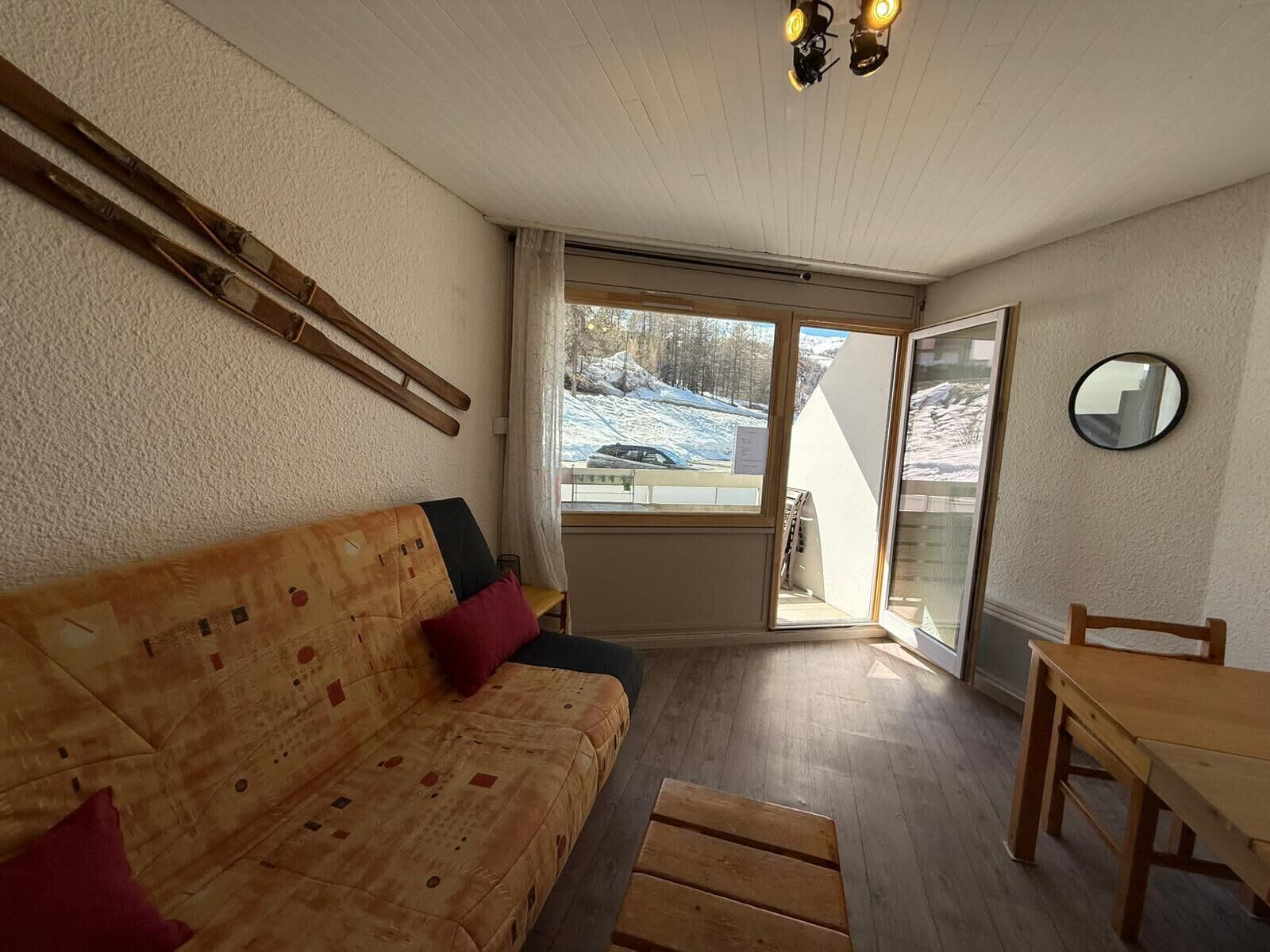 Una habitación acogedora con un sofá de madera, una mesa de comedor y vistas a un paisaje nevado a través de un ventanal grande.