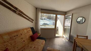 Una habitación acogedora con un sofá de madera, una mesa de comedor y vistas a un paisaje nevado a través de un ventanal grande.