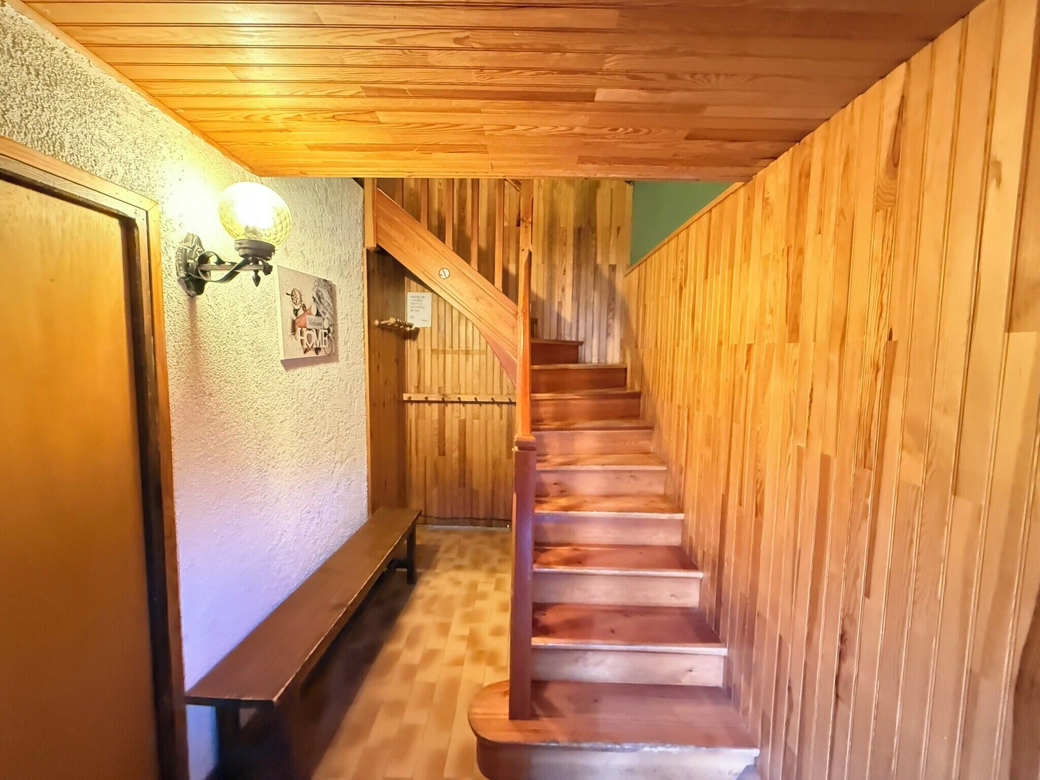 A wooden staircase with a bench at the bottom, a wall-mounted light fixture, and a door on the left.