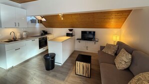 A modern kitchen with white cabinets, a built-in oven, and a dining area with a wooden table and bench. - Appart 6 pers - proche pistes et vue montagne (Vars)