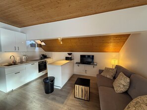 A modern kitchen with white cabinets, a built-in oven, and a dining area with a wooden table and bench. - Appart 6 pers - proche pistes et vue montagne (Vars)