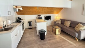 A modern kitchen with white cabinets, a wooden ceiling, a dining area with a grey sofa and patterned cushions, and a small side table. - Appart 6 pers - proche pistes et vue montagne (Vars)