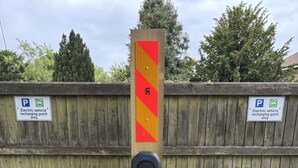 Een houten paal met een rood-geel gestreept bord en een parkeerschild met een oplaadpunt voor elektrische voertuigen.