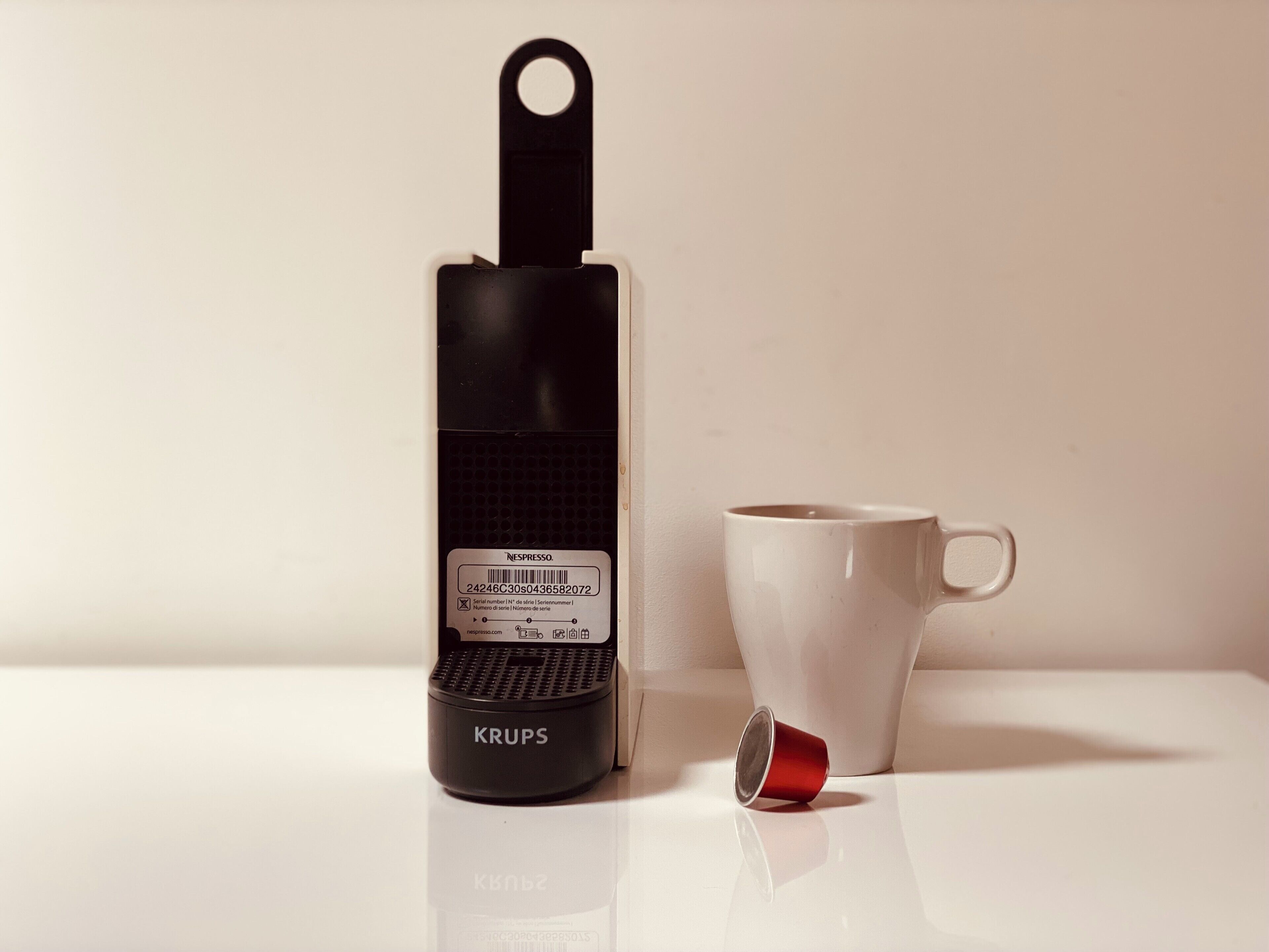 A black and white coffee maker with a label and a red cup beside it.