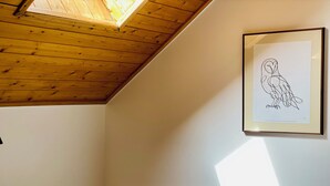 Una habitación con techo de madera, un dibujo enmarcado de un búho en la pared y un escritorio con una silla.