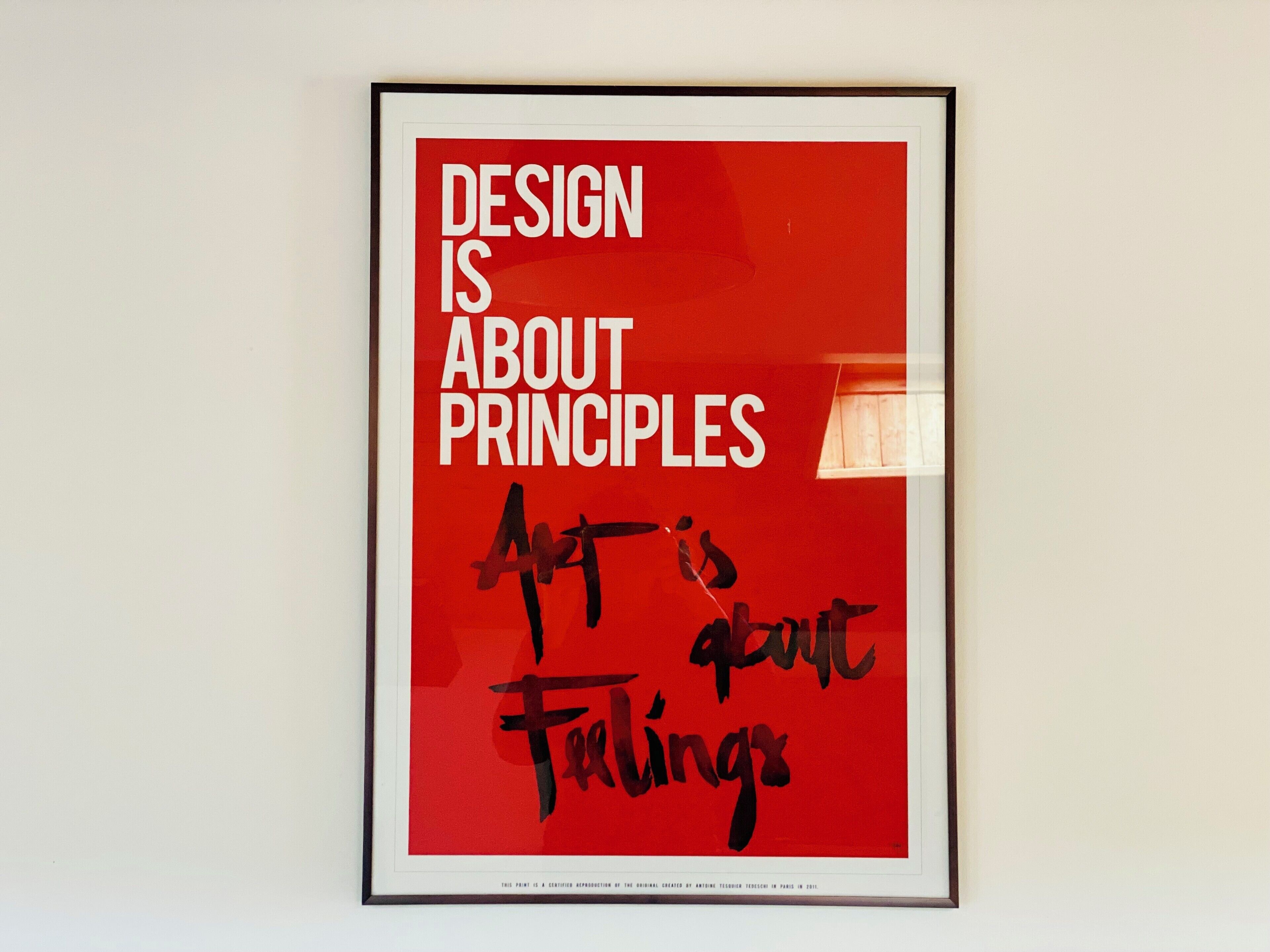 A framed poster with the text 'DESIGN IS ABOUT PRINCIPLES' and 'Art is about feelings' on a red background.