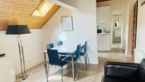 Un espacio habitable moderno con comedor, un sofá de cuero negro, una lámpara de pie y una cocina al fondo.