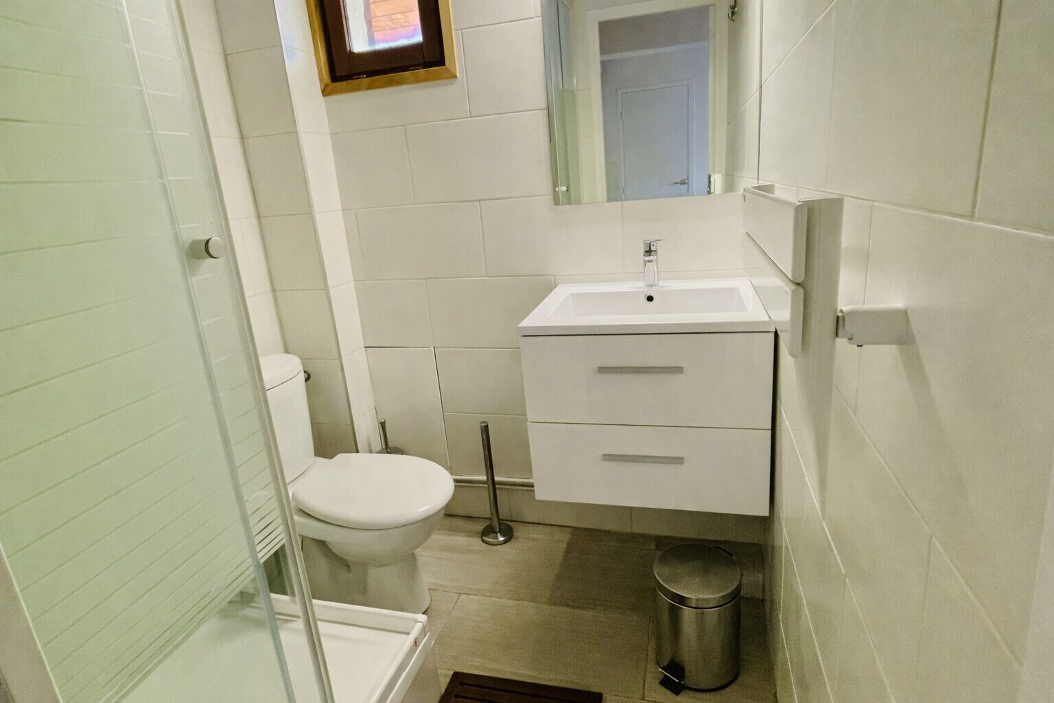 A small bathroom with a toilet, a sink, a mirror, and a trash can.