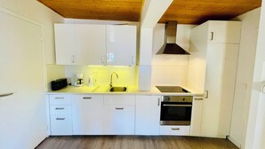 Uma cozinha compacta com armários brancos, pia de aço inoxidável, fogão a gás e forno embutido.