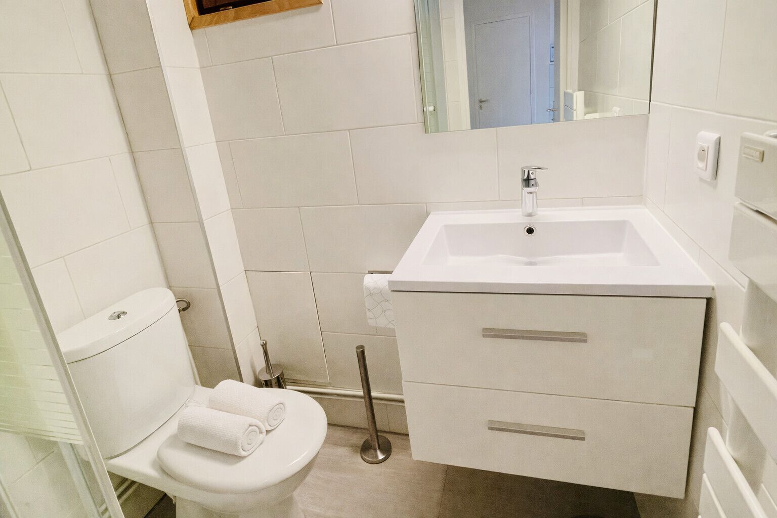 Un baño con inodoro blanco, lavamanos con espejo y una toalla en el inodoro.