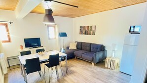 Un salon moderne comprenant un coin repas, un canapé gris, un réfrigérateur blanc et un téléviseur à écran plat.