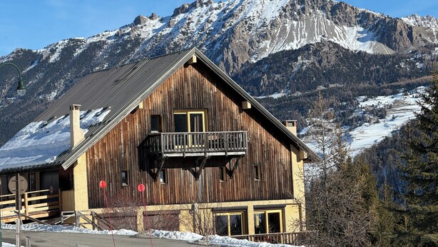 Un chalet en bois doté d’un balcon, situé au pied de montagnes enneigées.