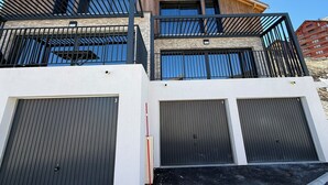 Un edificio de varios pisos con fachada de madera, un balcón con barandillas negras y tres puertas de garaje.