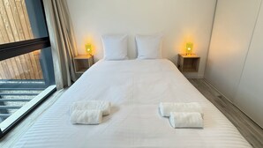 Habitación de hotel con una cama grande, dos lámparas de noche, una ventana con cortinas y dos toallas sobre la cama.