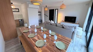 Un comedor moderno con una mesa de madera dispuesta para seis personas, un sofá, un televisor y una escalera que sube a otro nivel.