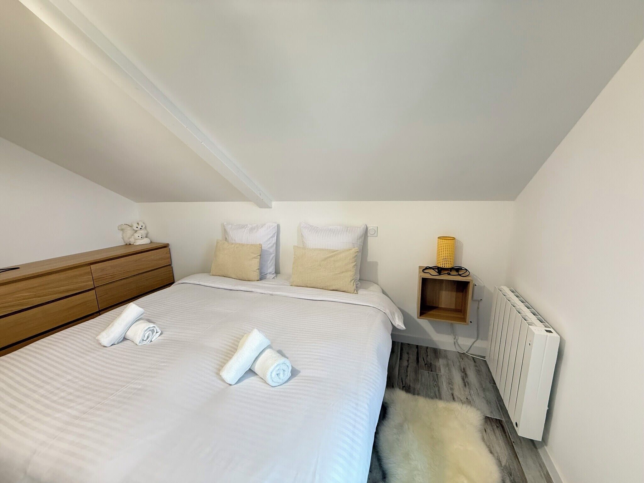 Ein Schlafzimmer mit einem Bett, Kissen, einem Nachttisch aus Holz, einer Lampe und einer Heizung.