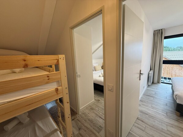 Une chambre avec un lit superposé, une porte donnant sur une autre chambre et une vue sur un balcon.