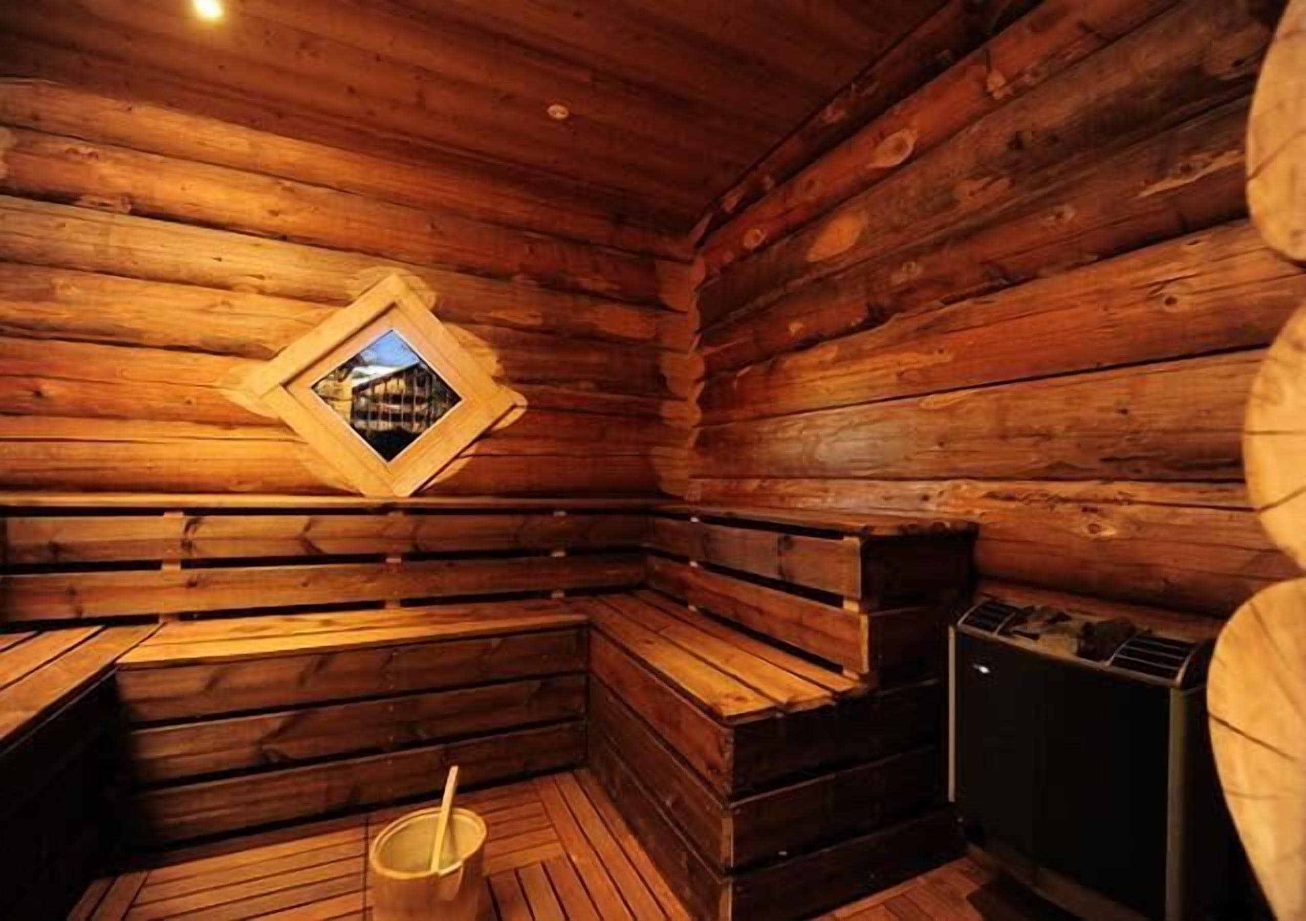 A sauna with wooden walls, a bench, a bucket, and a sauna heater.