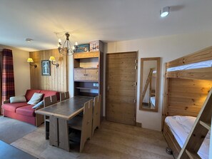 Habitación pequeña con literas, un sofá, una mesa de comedor y un armario de madera.