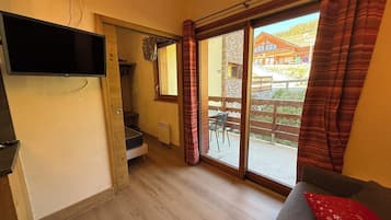 A room with a television mounted on the wall, a sliding door leading to an outdoor area, and a sofa with a red cushion.
