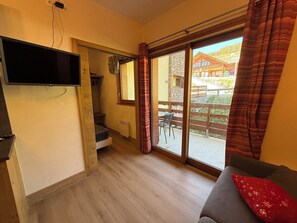 Ein Zimmer mit an der Wand montiertem Fernseher, einer Schiebetür zu einem Außenbereich und einem Sofa mit rotem Kissen.