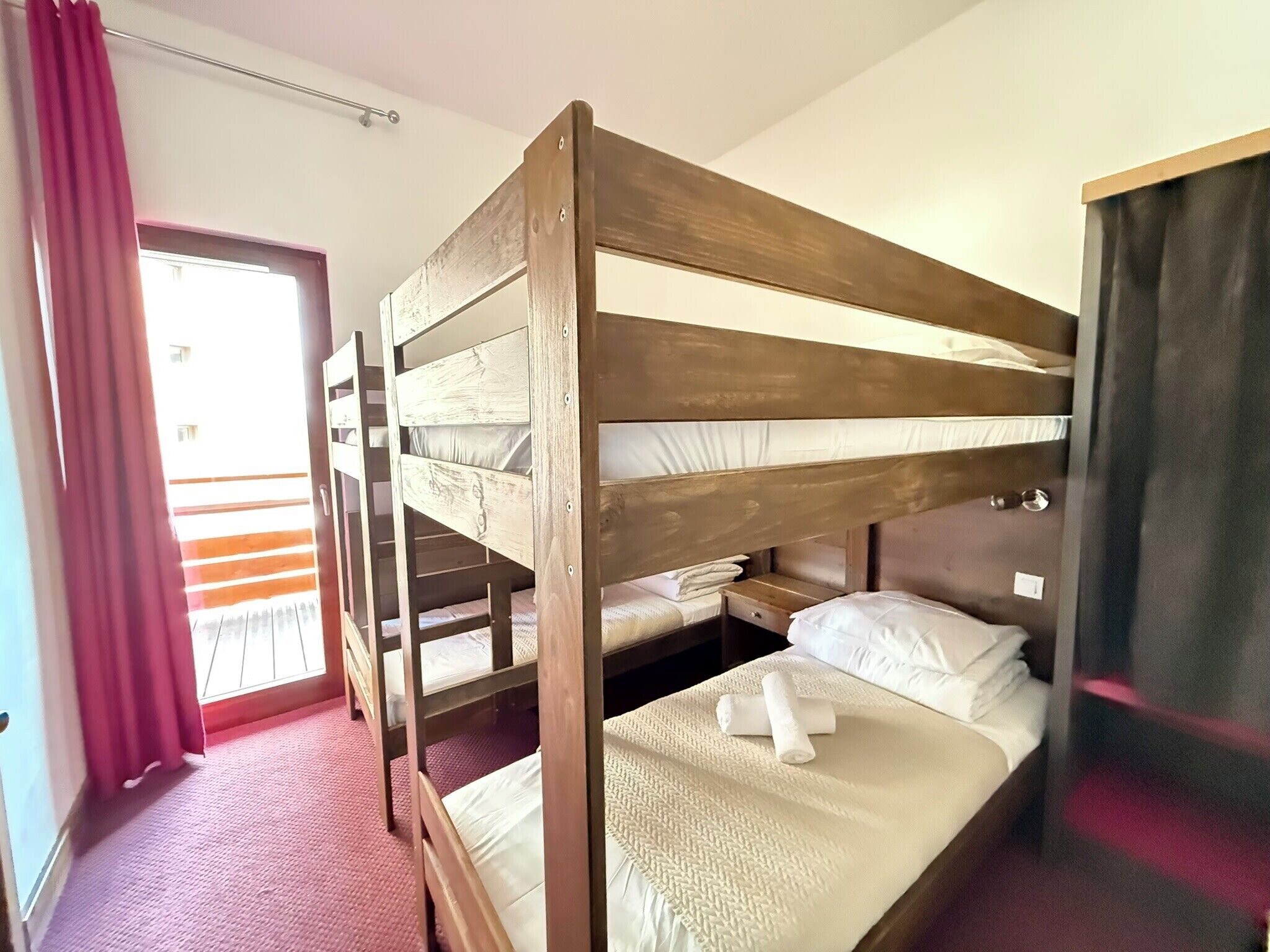 A bunk bed room with a window, a door, and a red curtain.