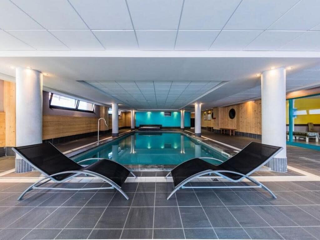 An indoor swimming pool with black lounge chairs, a wooden wall, and a blue accent wall.