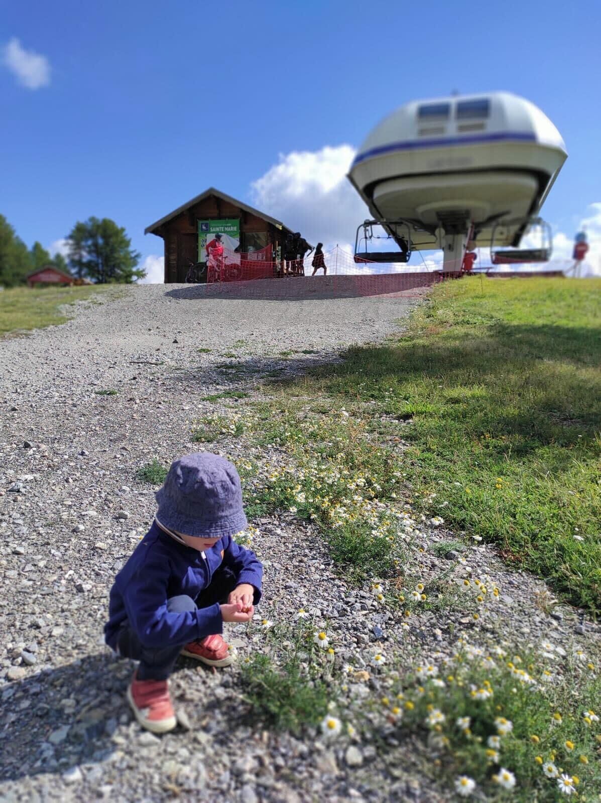 A child playing on a gravel path with a grassy area and a building in the background.
