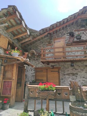 A rustic stone building with wooden doors and a wooden bench with flowers. - Chalet familial • 3 chambres • Jardin 600 m² • Vars (Vars)