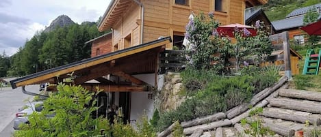 Una cabaña de madera con techo inclinado, un balcón de madera y montañas al fondo.
