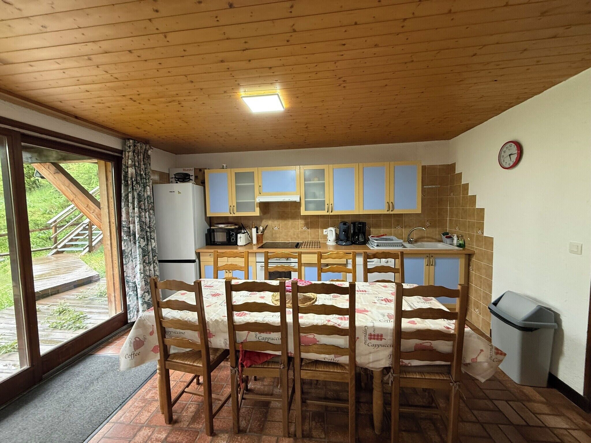 Une cuisine avec des meubles de rangement en bois, un réfrigérateur, un évier et une table à manger avec des chaises.