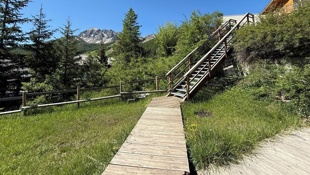 Ein hölzerner Pfad führt zu einer Treppe, vor dem Hintergrund Berge.