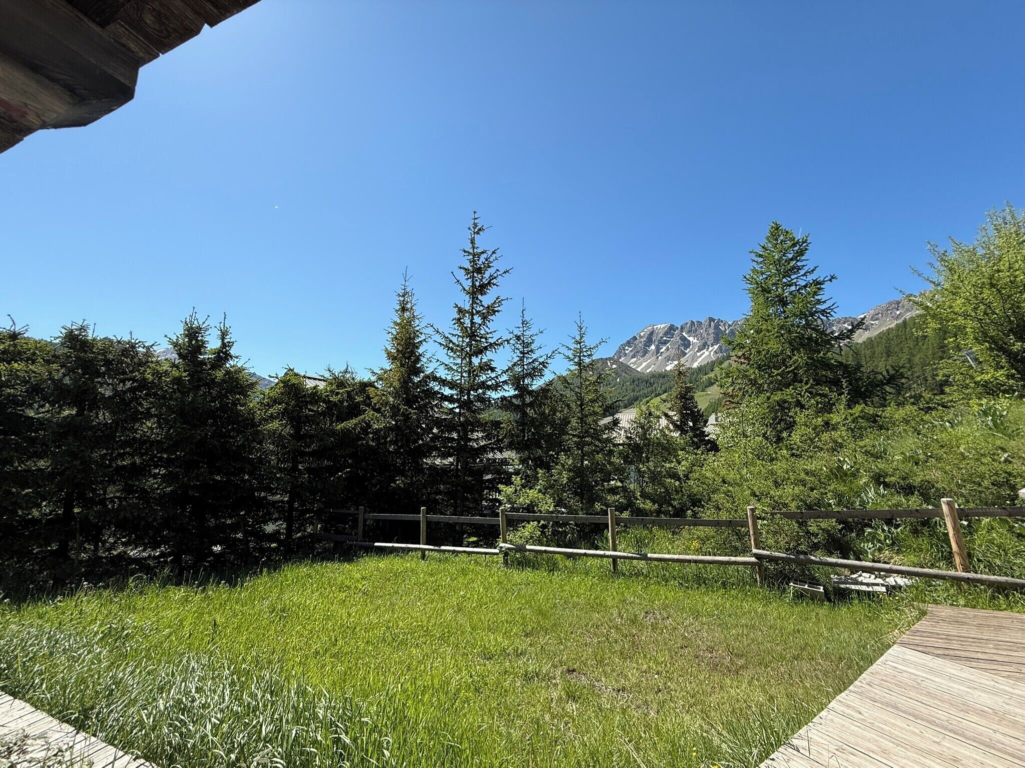 Une zone herbeuse bordée d’une clôture en bois, avec une chaîne de montagnes en arrière-plan.