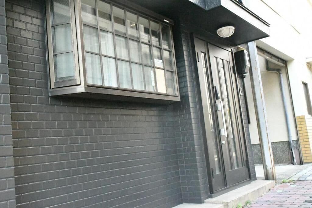 A building with a black brick facade, a large window with multiple panes, and a door with a black frame.