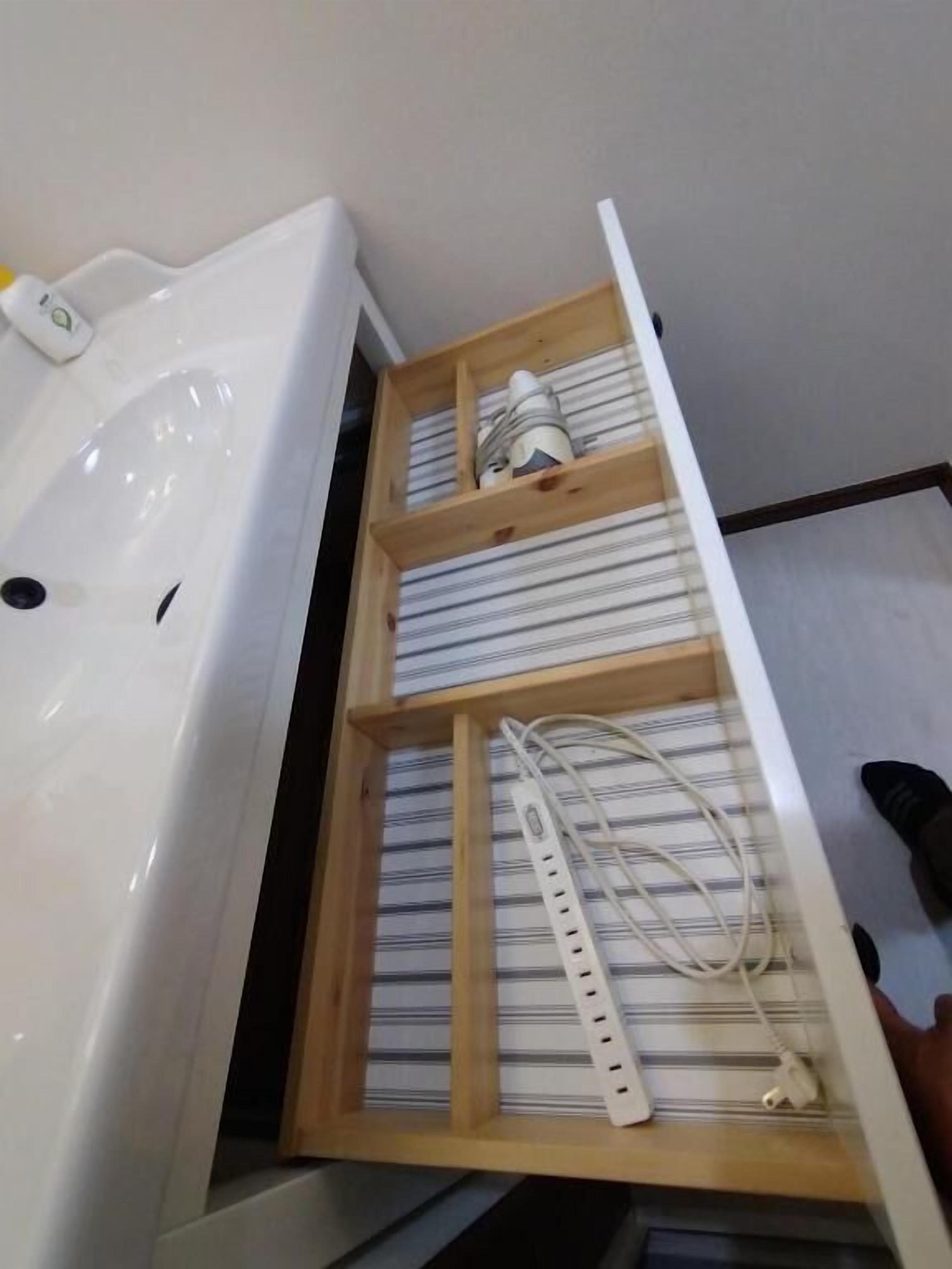 A bathroom with a white sink, a wooden shelf with striped towels, and a white power strip.