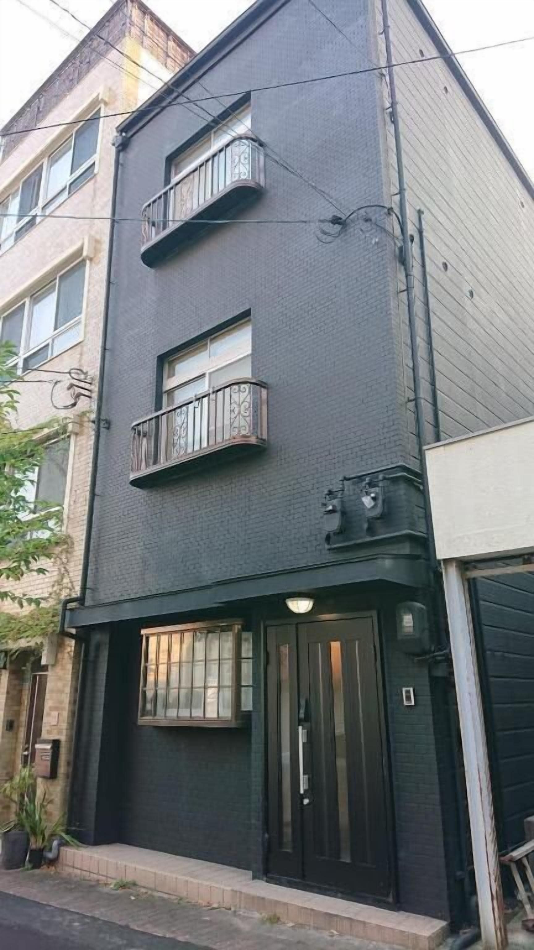 A multi-story building with a dark facade, a front door, and two balconies.