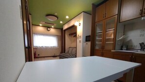 A compact kitchen with a white countertop, wooden cabinets, and a small refrigerator. - Kobe Family House near Motomachi (Kobe)