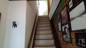 A staircase with a wooden handrail and a chair on the left. - Kobe Family House near Motomachi (Kobe)