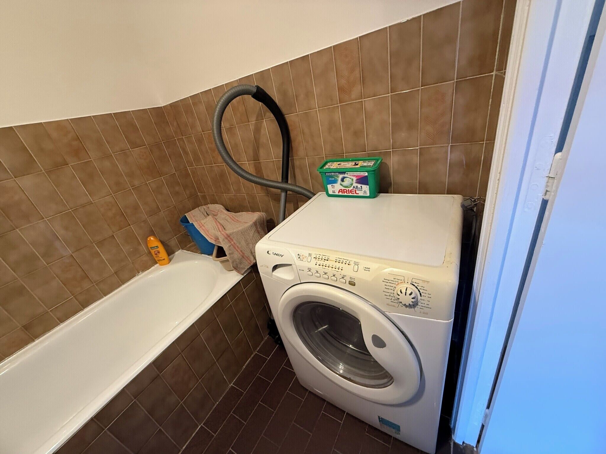 Un área de lavandería con lavadora, bañera y manguera.