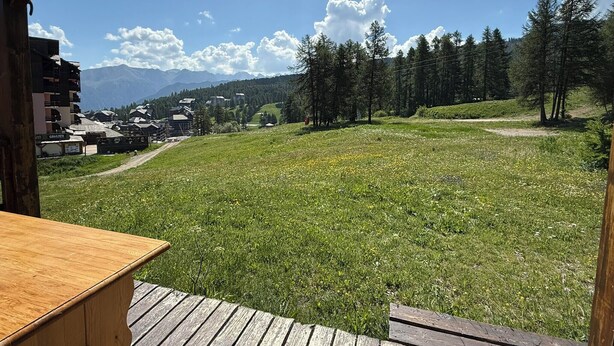 Eine Holzterrasse mit Blick auf ein Wiesfeld, Bäume und Gebäude in der Ferne.