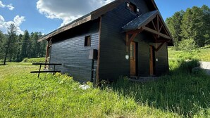Eine rustikale Holzhütte mit geneigtem Dach und einer Bank im Vordergrund.