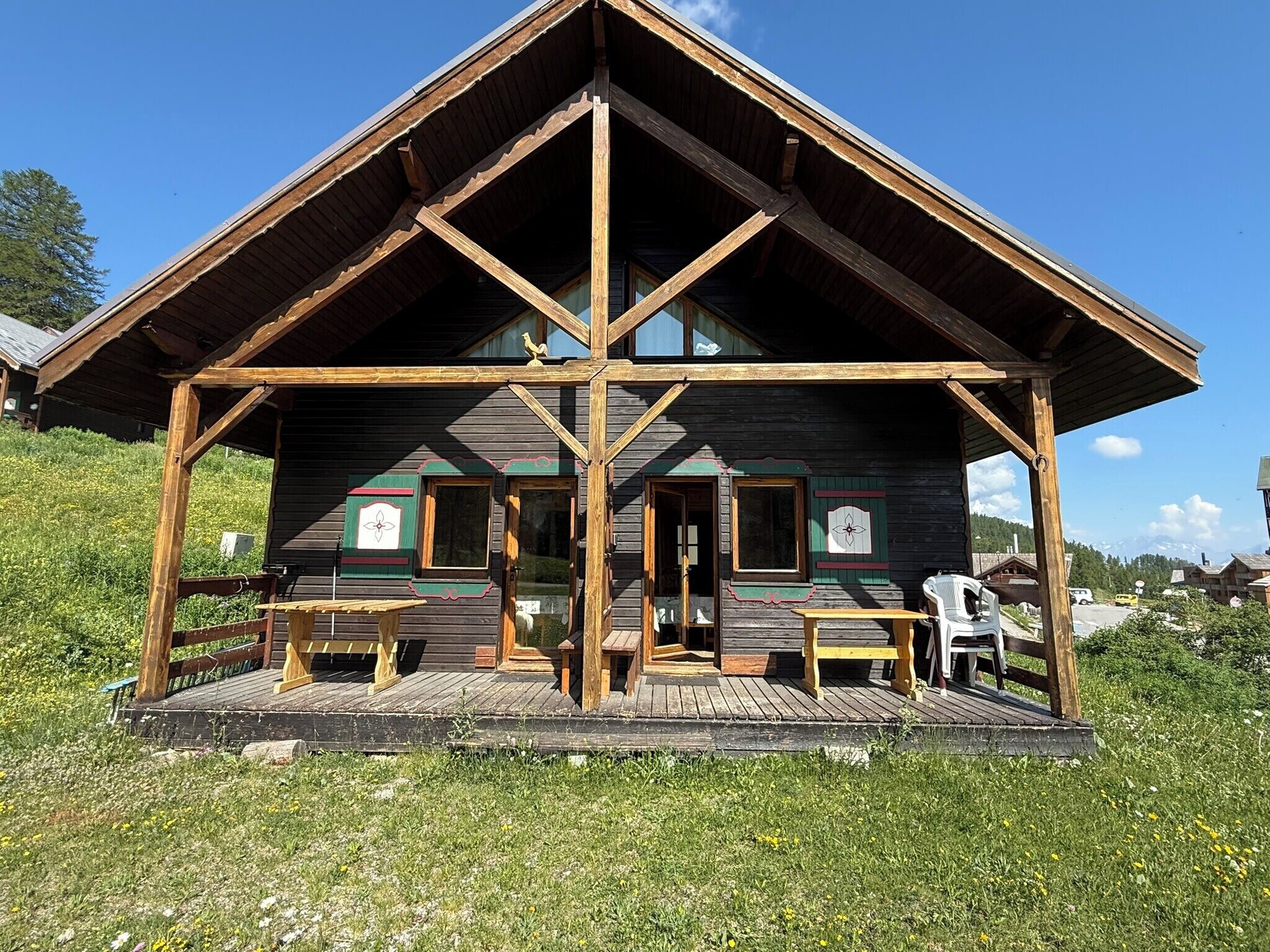 A wooden chalet with a balcony, wooden benches, and a view of the surrounding landscape.