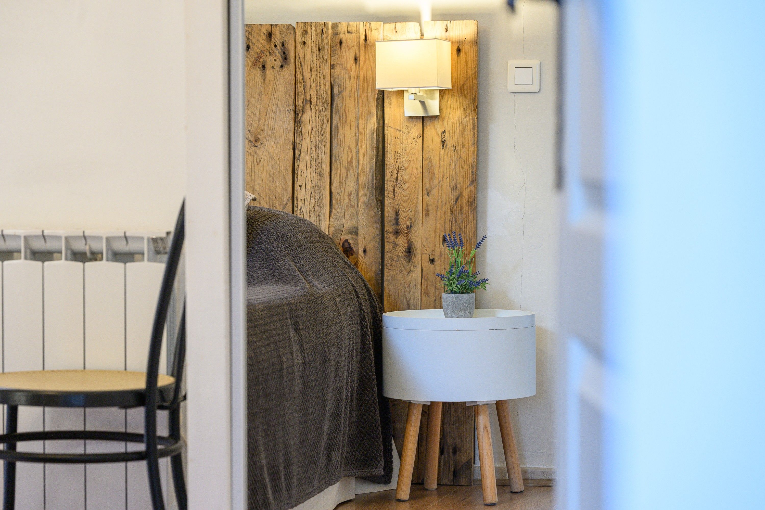 A room with a bed, a bedside table with a lamp, and a chair.