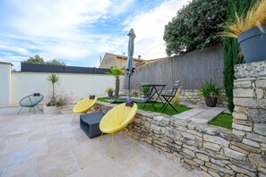 Une terrasse avec un sol en pierre, des chaises jaunes, une table et un mur en pierre.