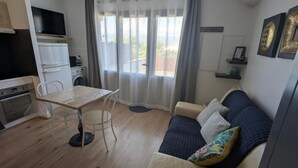 Un espacio habitable compacto con kitchenette, una mesa de comedor, un sofá y un amplio ventanal con cortinas.